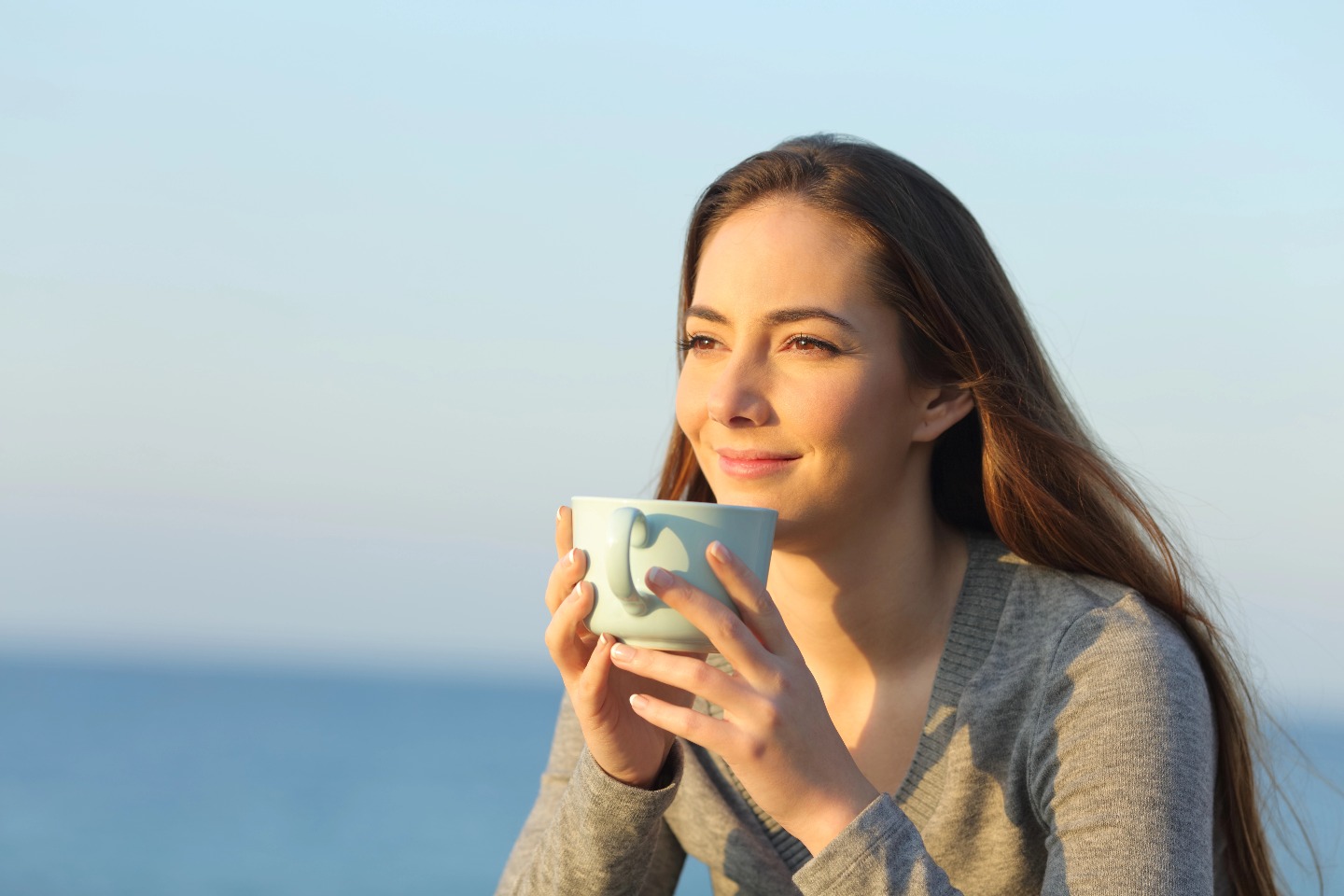 Relaxed woman drinking coffee looking at horizon on the beach at sunset